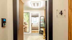 A hotel room entrance with a digital lock, a number '4' sign, a bed, a bedside table, a mirror, and a small plant. - Bellavia Deluxe Apart (Istanbul)