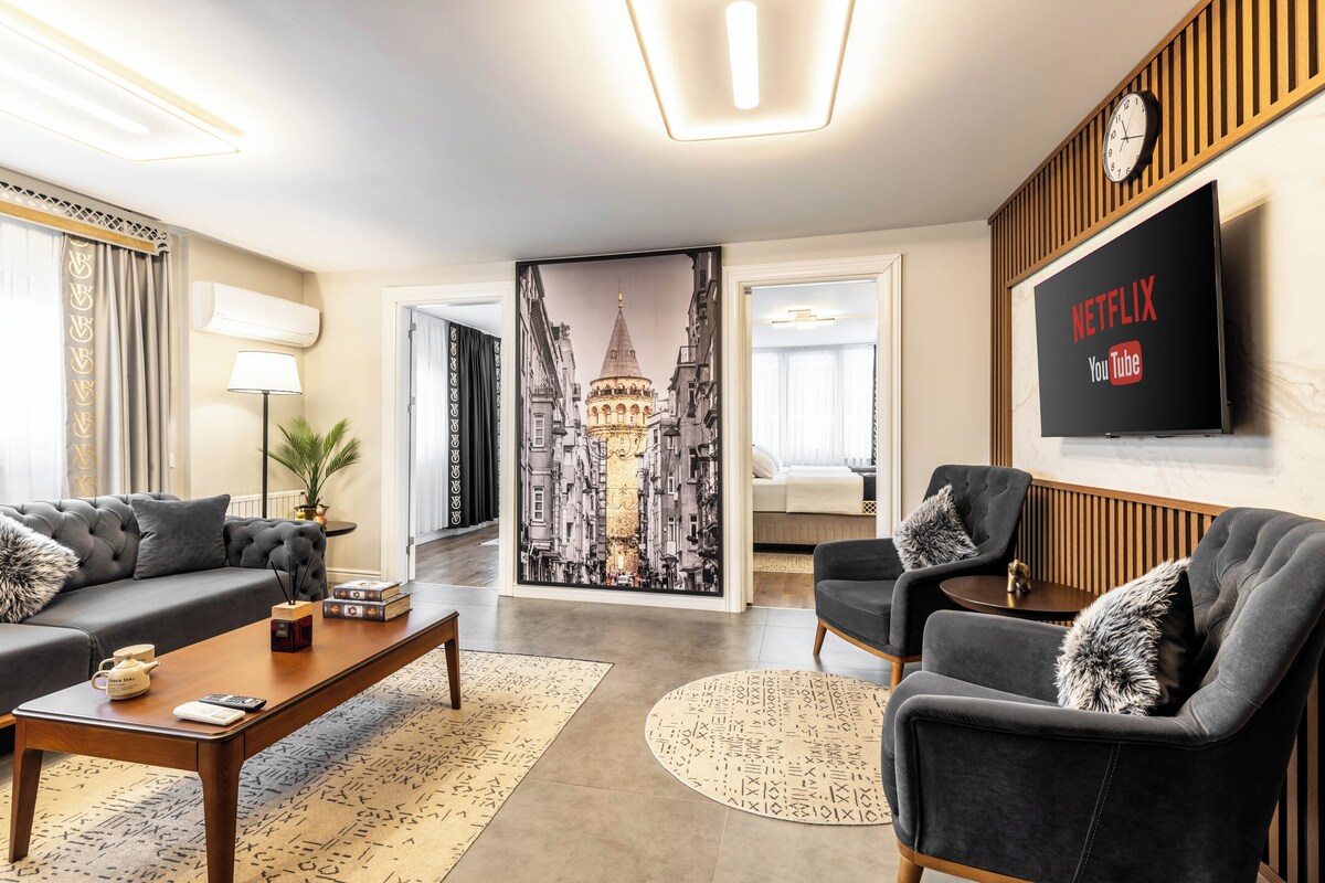 Ein modernes Wohnzimmer mit einer Couch, Sesseln, einem Couchtisch und einem an der Wand befestigten Fernseher.