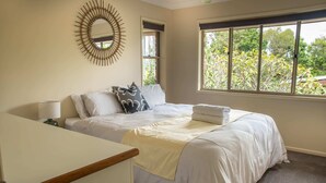 Quarto com cama, mesa de cabeceira, abajur, janela com vista para árvores e espelho fixado na parede.