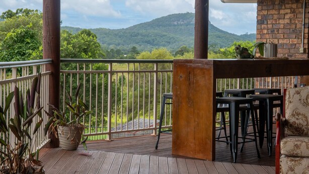 Um deck de madeira com guarda-corpo, uma mesa com cadeiras e um vaso com planta.