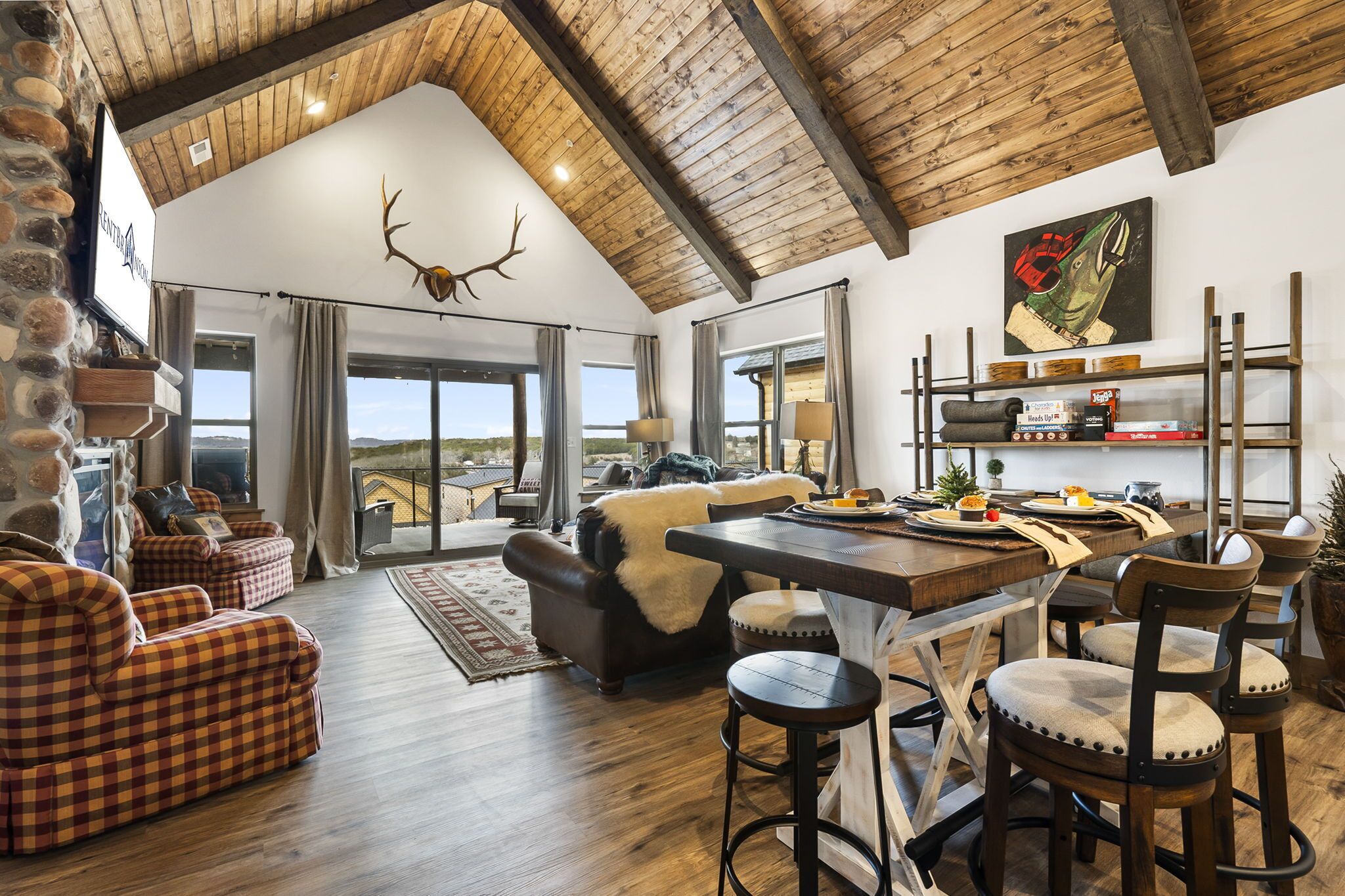 A spacious living area with a high wooden ceiling, a fireplace, and a large window offering a view of the landscape.