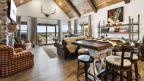 A spacious living area with a high wooden ceiling, a fireplace, and a large window offering a view of the landscape.