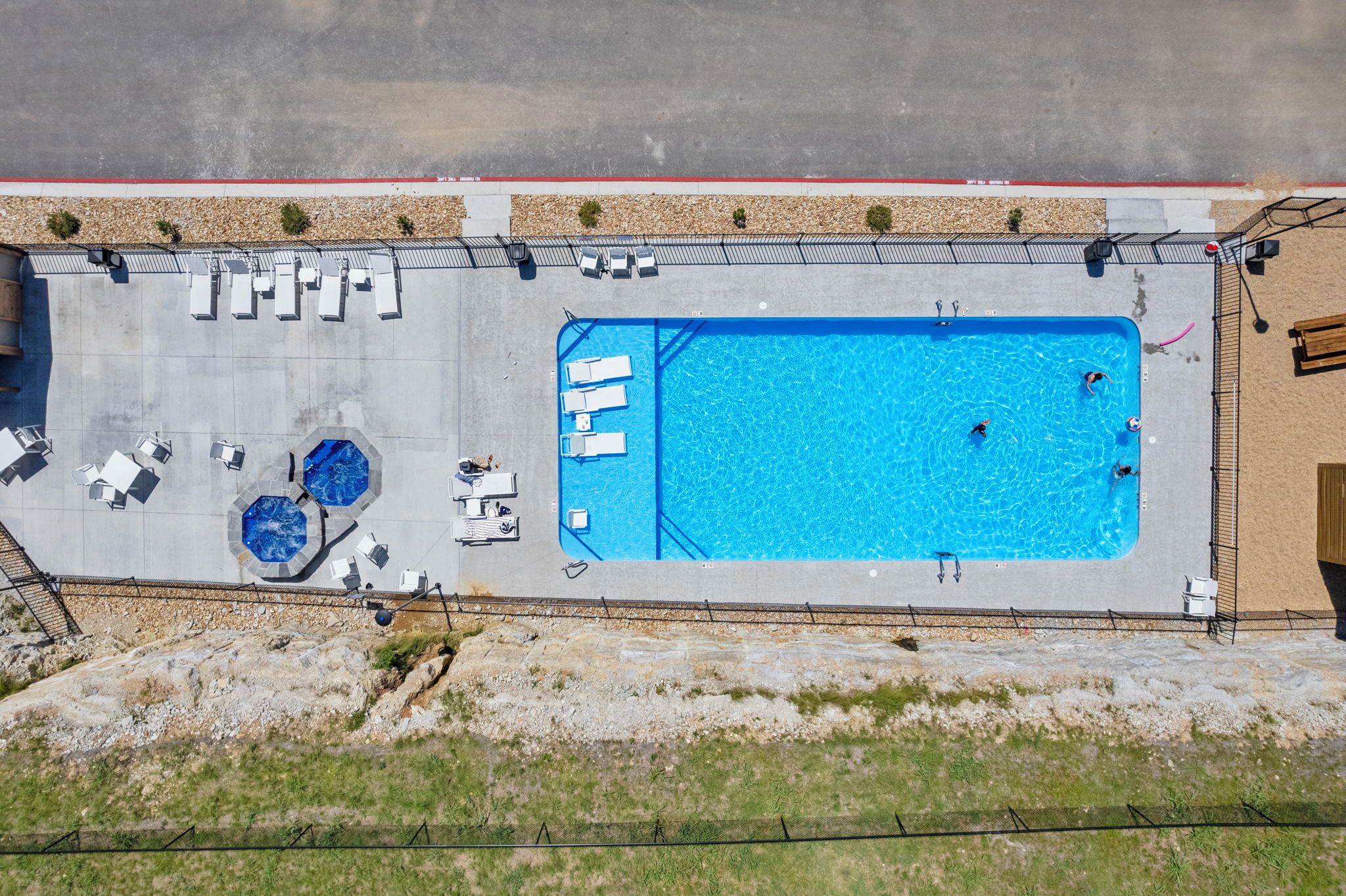 An aerial view of a swimming pool with lounge chairs and a small hot tub area.