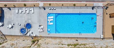 An aerial view of a swimming pool with lounge chairs and a small hot tub area.