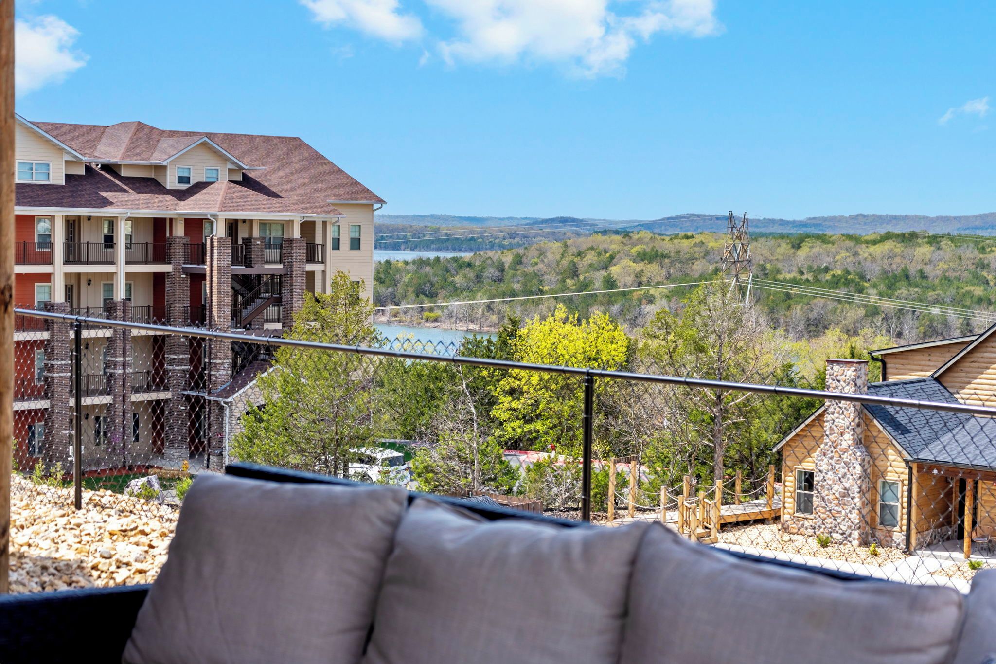 A balcony with a view of a lake, a multi-story building, and a stone cabin.