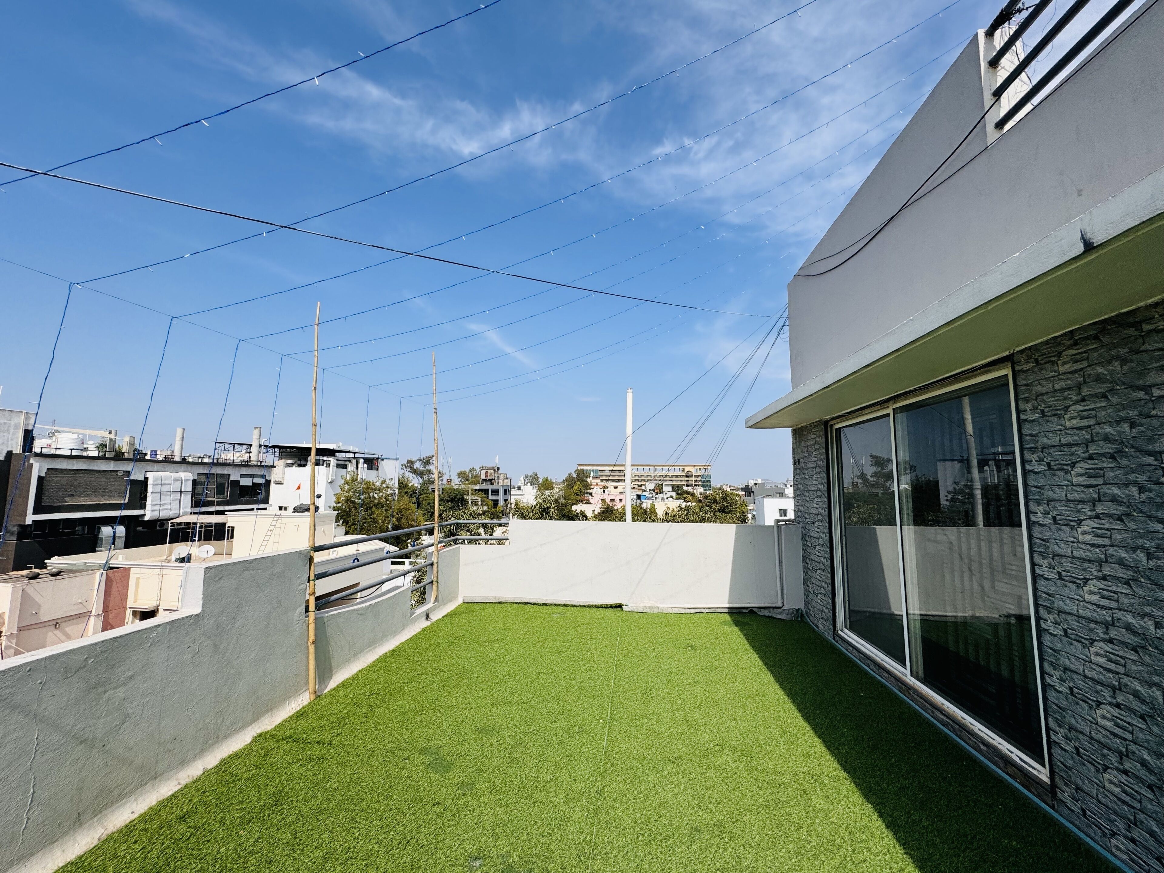 A rooftop with artificial grass, a stone wall, and a modern building with large windows.