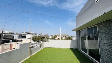 A rooftop with artificial grass, a stone wall, and a modern building with large windows.