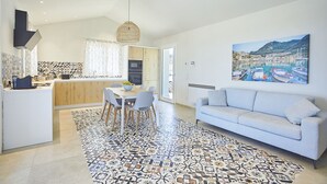 A modern kitchen with a dining area, a sofa, and a large painting of a coastal scene.