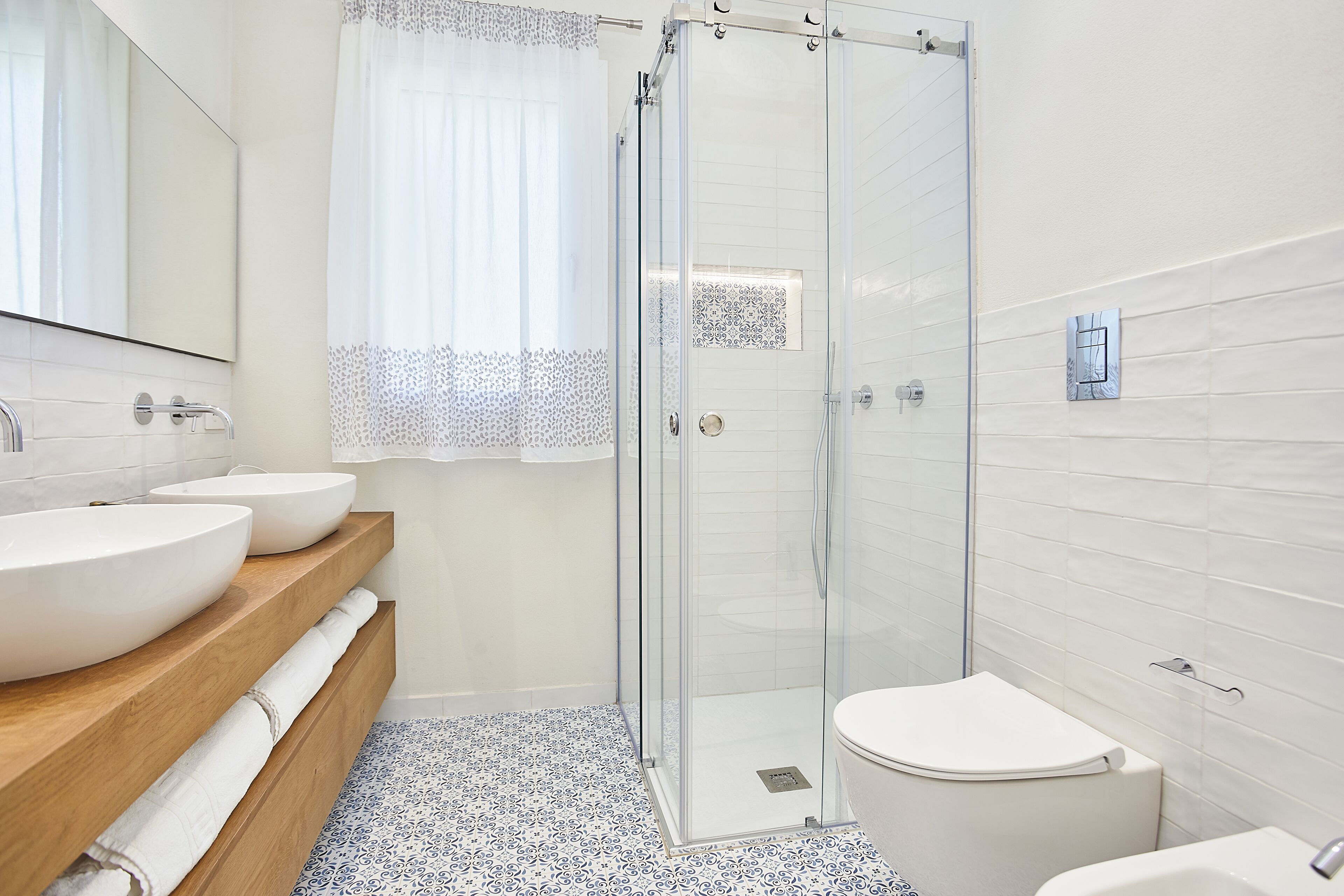 Un baño moderno con cabina de ducha de vidrio, dos lavamanos y un inodoro.