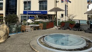 A modern building with a casino named "CASINO ADMIRAL" and a pool area with lounge chairs and umbrellas. - Britain in the Sun at Luxurious Ocean Village (Gibraltar)