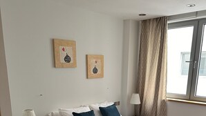 A modern bedroom with a large bed, a nightstand, a lamp, and two wall-mounted artworks. - Britain in the Sun at Luxurious Ocean Village (Gibraltar)
