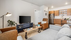 Un salon moderne avec un téléviseur à écran plat, une table basse et un canapé. Il y a également un coin cuisine avec des meubles en bois et des appareils électroménagers en acier inoxydable.