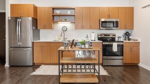 Une cuisine moderne avec des meubles en bois, des appareils électroménagers en acier inoxydable, un îlot central et une horloge au mur.