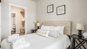 Un lit bien fait, avec du linge de lit blanc, une table de chevet avec une lampe et une horloge fixée au mur.