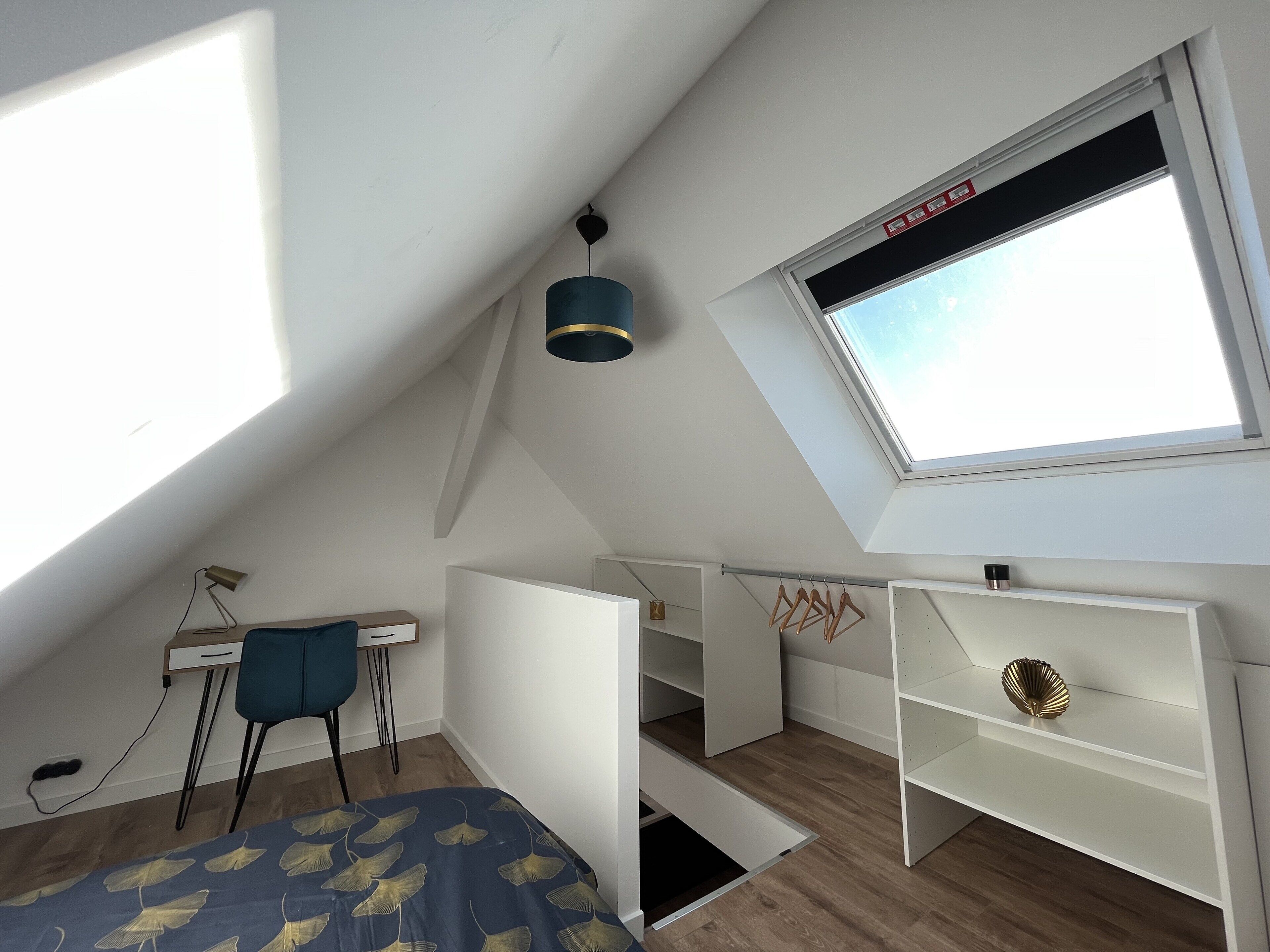 Un dormitorio abuhardillado pequeño y bien iluminado, con un tragaluz, un escritorio y una silla.