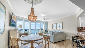 A spacious living area with a round wooden table, comfortable seating, a large window with a view, and a ceiling fan. - Family-Friendly Two Bedroom Unit with Phenomenal Gulf and Bay Views. Complimentary Boat Slip! (Orange Beach)