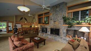 A spacious living room with a stone fireplace, a ceiling fan, and a television.