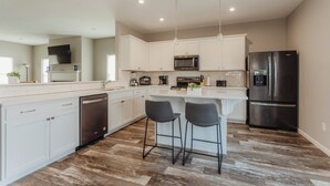 A modern kitchen with white cabinets, a stainless steel refrigerator, a microwave, and two bar stools. - Heated Private Pool, Spacious, Hot Tub All Year (New Buffalo)