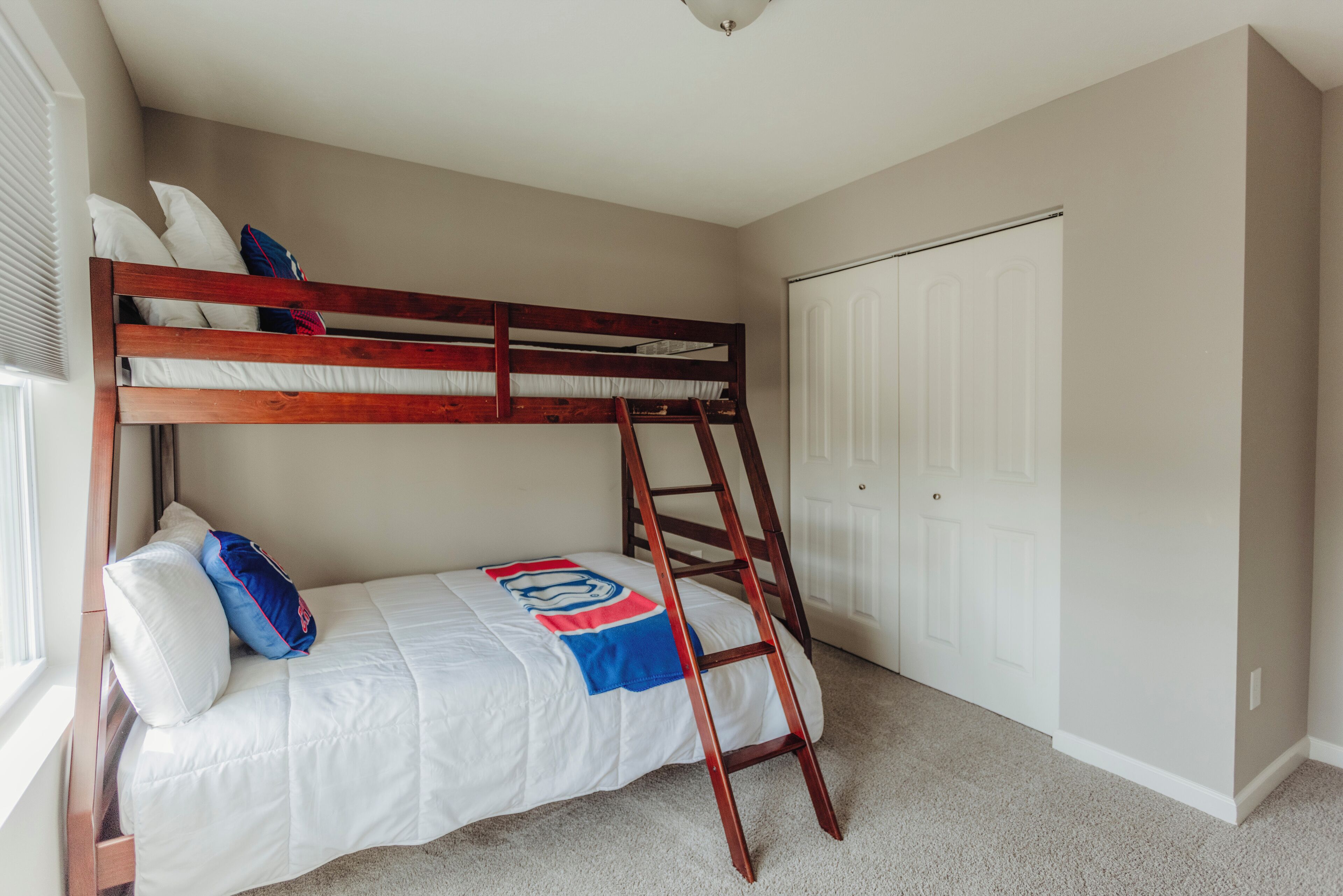 A bunk bed with a ladder, a white door, and a window with blinds.