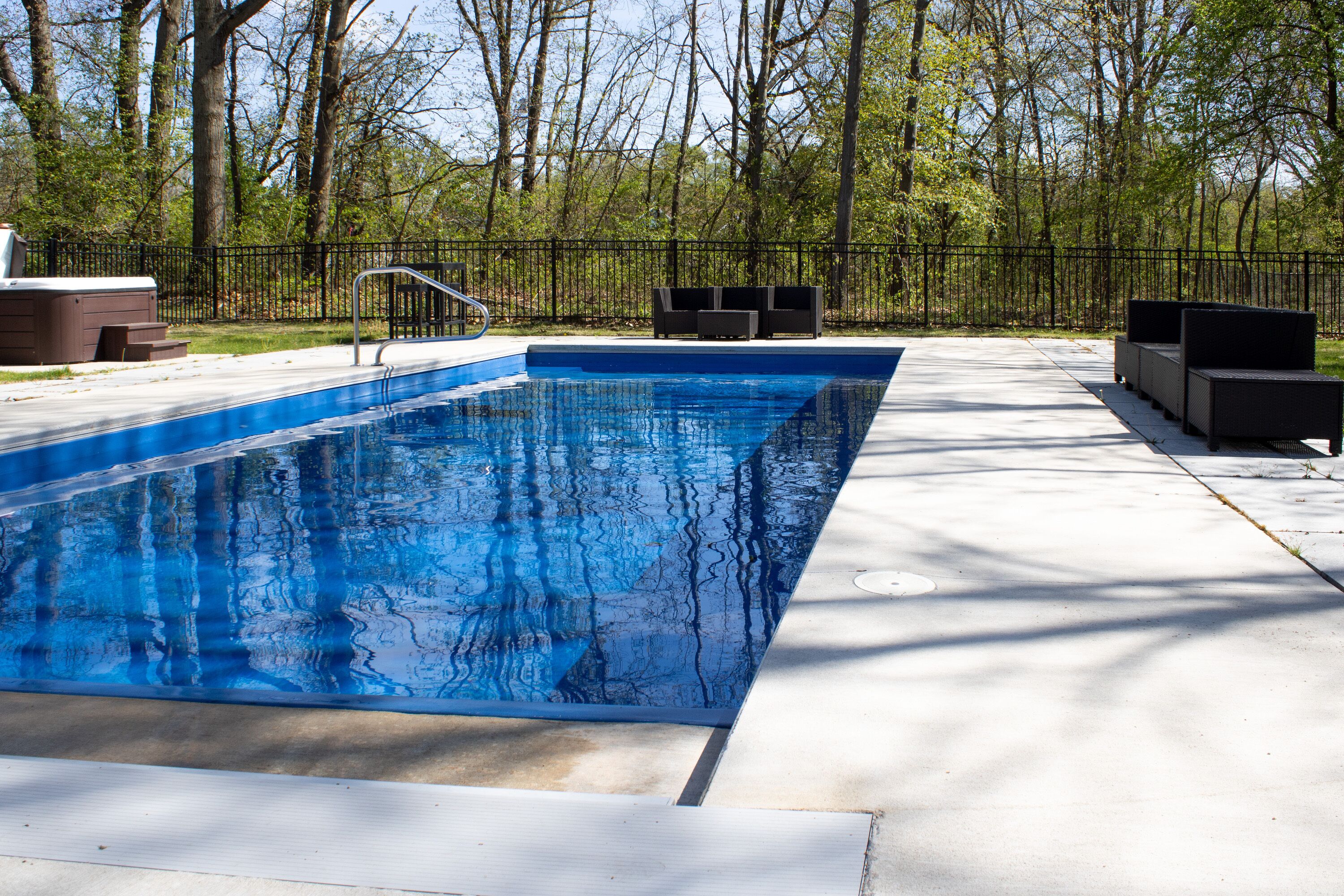 A rectangular swimming pool with a clear blue water surface, surrounded by a concrete deck.