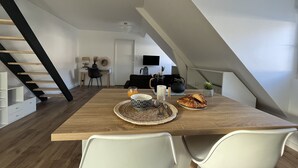 A modern kitchen with a wooden table, white chairs, and a staircase. - Studio Scandinave - Duplex - Hyper Centre (Lorient)
