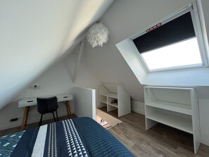 A modern, well-lit attic bedroom with a sloped ceiling, a skylight, a bed with a patterned bedspread, a desk, and built-in shelving.