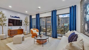 A modern living room with a sofa, armchair, coffee table, TV, and a cityscape view through large windows. - Dancing in the Moonlight in Downtown Nashville, Walk to Broadway (Nashville)