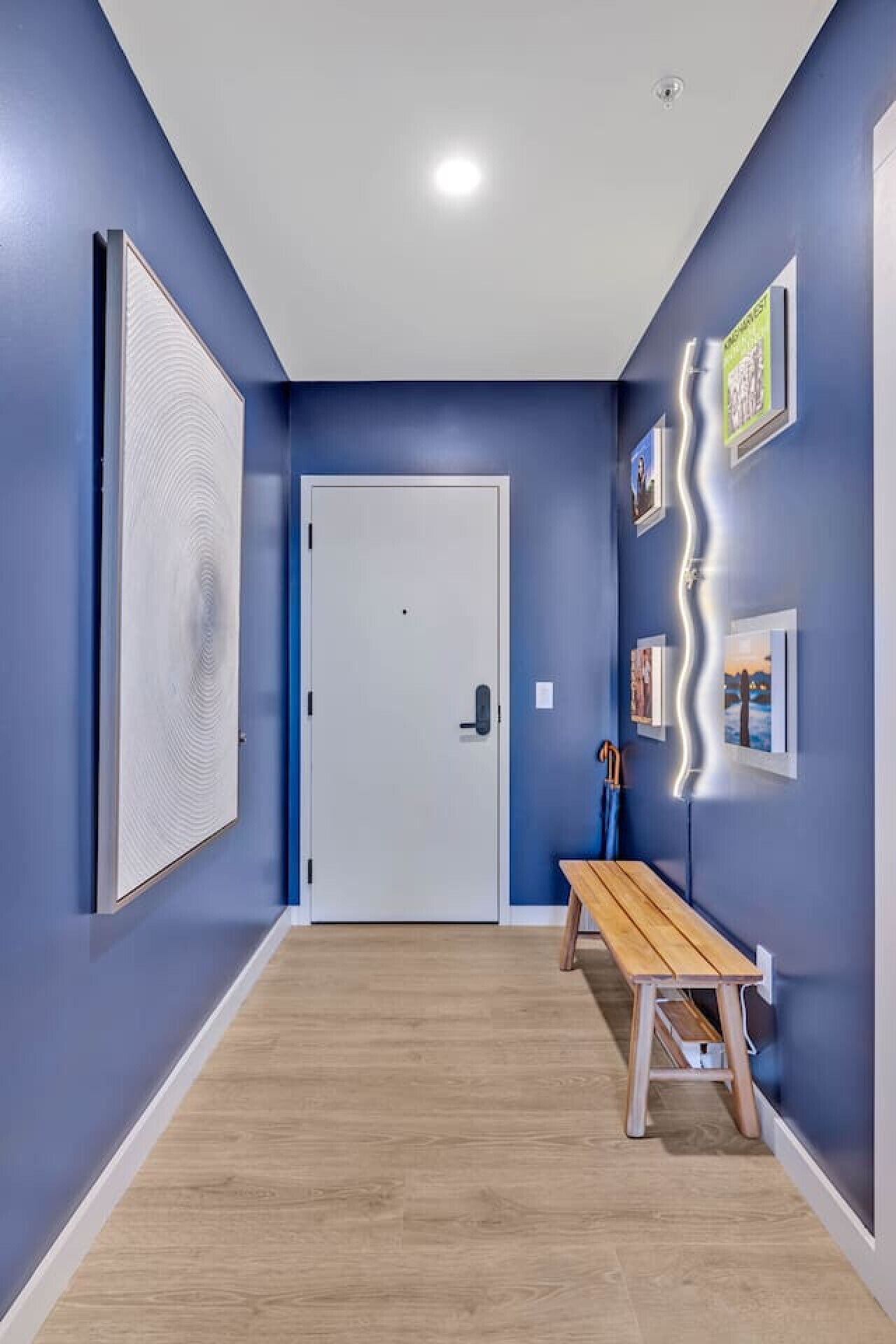 Een gang met blauwe wanden, een houten bank en een witte deur.