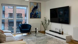 A modern living room with a large window, a blue armchair, a glass coffee table, a white entertainment unit, and a painting on the wall. - Stunning 2-bed Apartment in Dartford (Dartford)