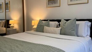 A neatly made bed with a white comforter and pillows, a bedside table with a lamp, and two framed artworks on the wall. - Stunning 2-bed Apartment in Dartford (Dartford)