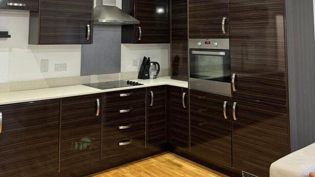 A modern kitchen with dark wood cabinets, stainless steel appliances, and a white countertop. - Stunning 2-bed Apartment in Dartford (Dartford)