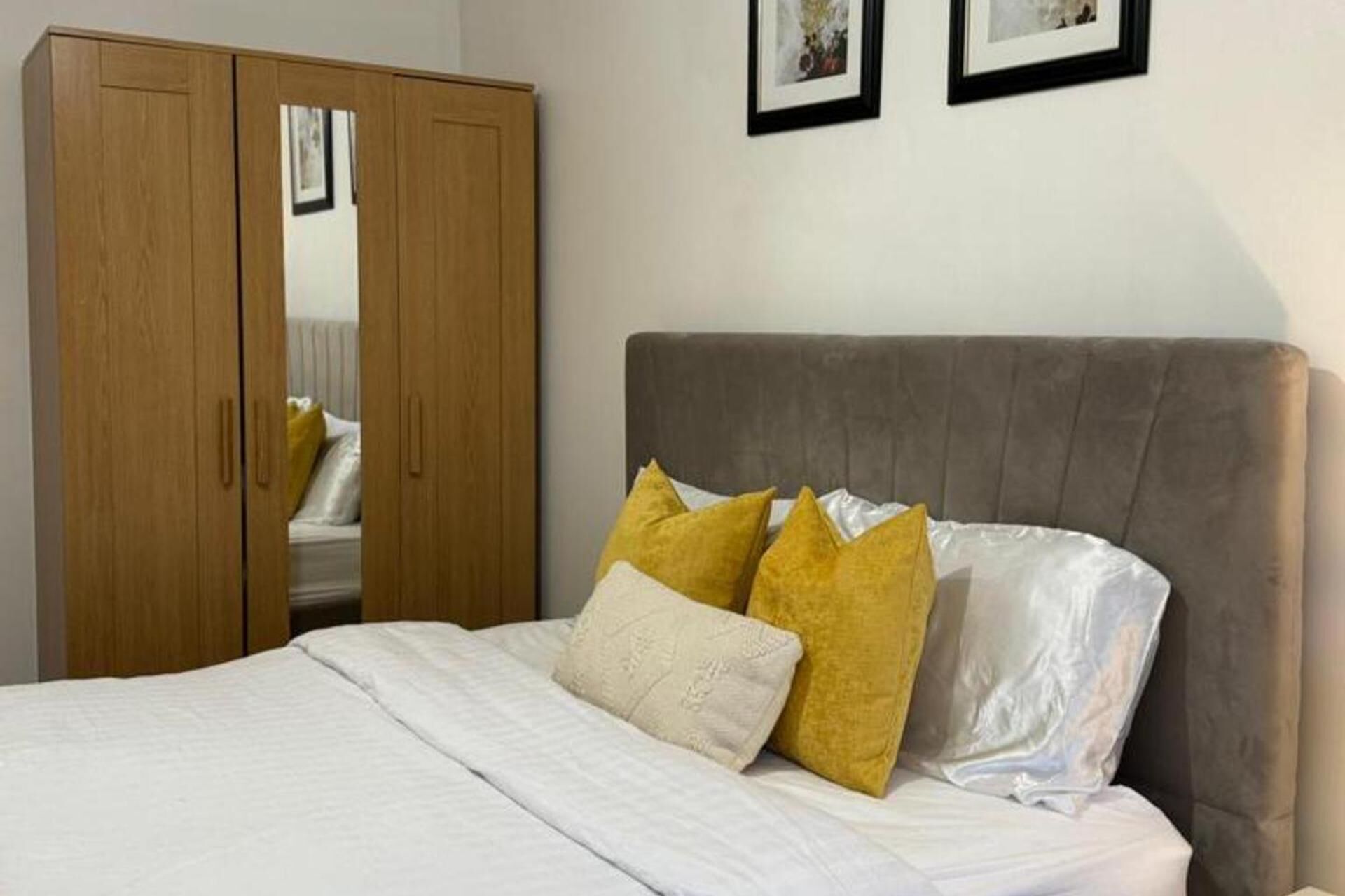 A bedroom with a bed, a wardrobe, and two framed pictures on the wall.
