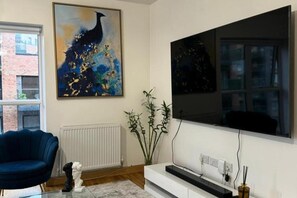 A living room with a blue armchair, a white fireplace, a large abstract painting, and a flat-screen TV mounted on the wall.