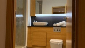 A modern bathroom with a wooden vanity, a white sink, and a toilet. - Stunning 2-bed Apartment in Dartford (Dartford)