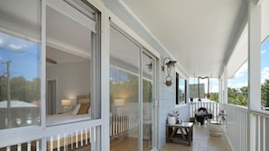Un balcón cubierto con puertas de vidrio, piso de madera y barandilla blanca.