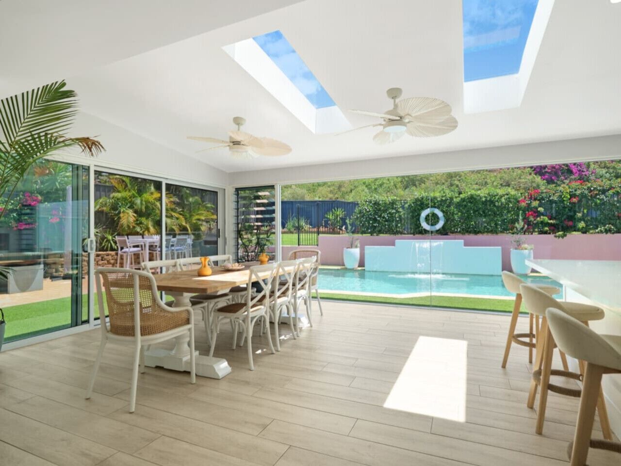 Un'area pranzo esterna moderna con piscina, ampie finestre e ventilatori a soffitto.