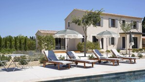 A poolside area with lounge chairs and umbrellas, a clear sky, and a building with a tiled roof. - Magnifique Maison à 5 mn de Saint Rémy de Provence Avec Piscine, Cuisine D'été (Graveson)