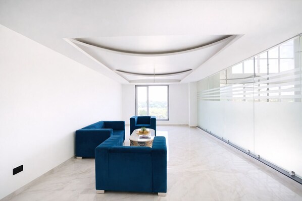 A spacious room with a modern ceiling design, a large window, and a seating area with blue sofas. - Hotel Holiday Grand Near Expo Mart (Greater Noida)