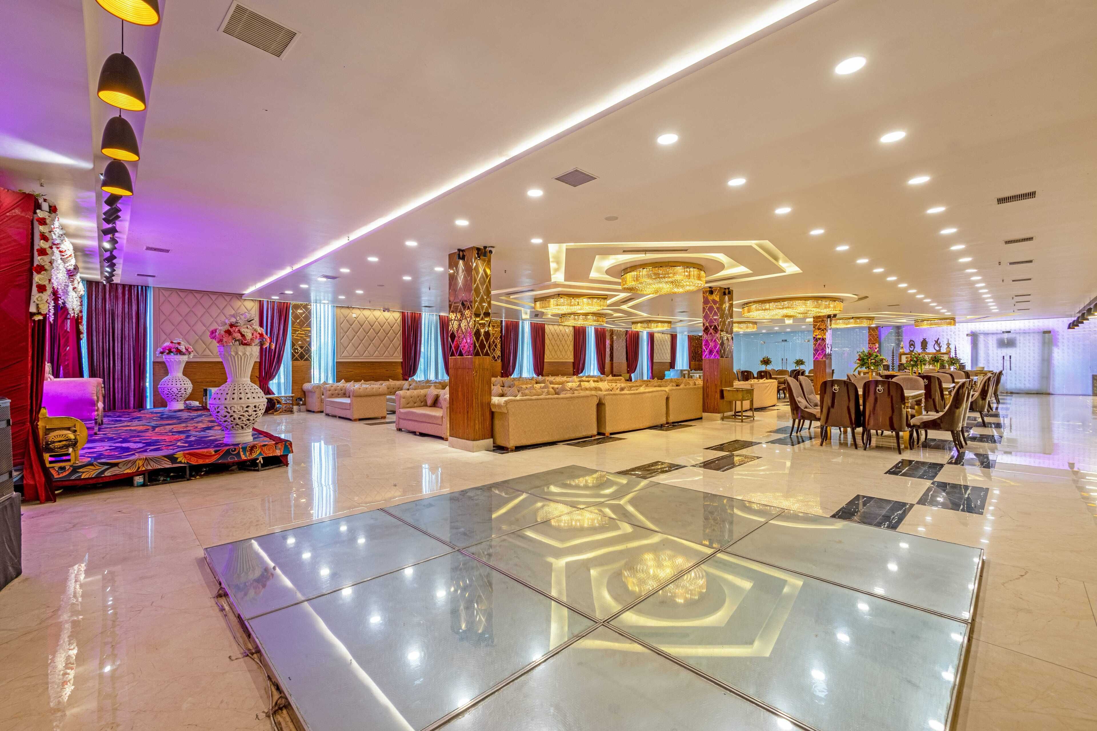 A spacious hotel lobby with a central reception desk, plush seating areas, and a decorative stage.