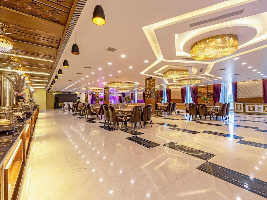 A spacious hotel lobby with a polished marble floor, elegant chandeliers, and a long reception desk.