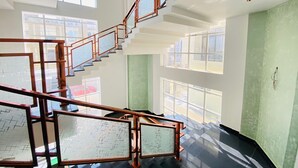 A spacious interior with a central staircase, large windows, and a green accent wall. - Hotel Holiday Grand Near Expo Mart (Greater Noida)