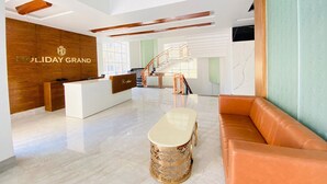 A modern hotel lobby with a reception desk, a staircase, and a seating area. - Hotel Holiday Grand Near Expo Mart (Greater Noida)