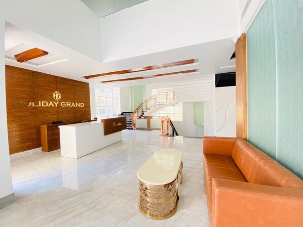A modern hotel lobby with a reception desk, a staircase, and a seating area. - Hotel Holiday Grand Near Expo Mart (Greater Noida)