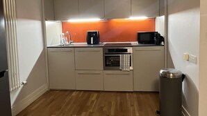 Een kleine keuken met een magnetron, koffiezetapparaat en een prullenbak.