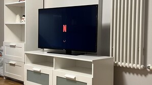 Een moderne woonkamer met een flatscreen televisie op een witte tv-meubel, een radiator en een houten vloer.