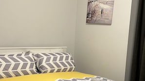 Een opgemaakt bed met patroonlinnen, een hoofdbord en een aan de muur bevestigd schilderij.