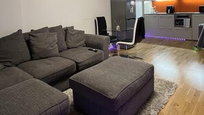 Een moderne woonkamer met een hoekbank, een poef en een bijzettafeltje met een zakdoos.