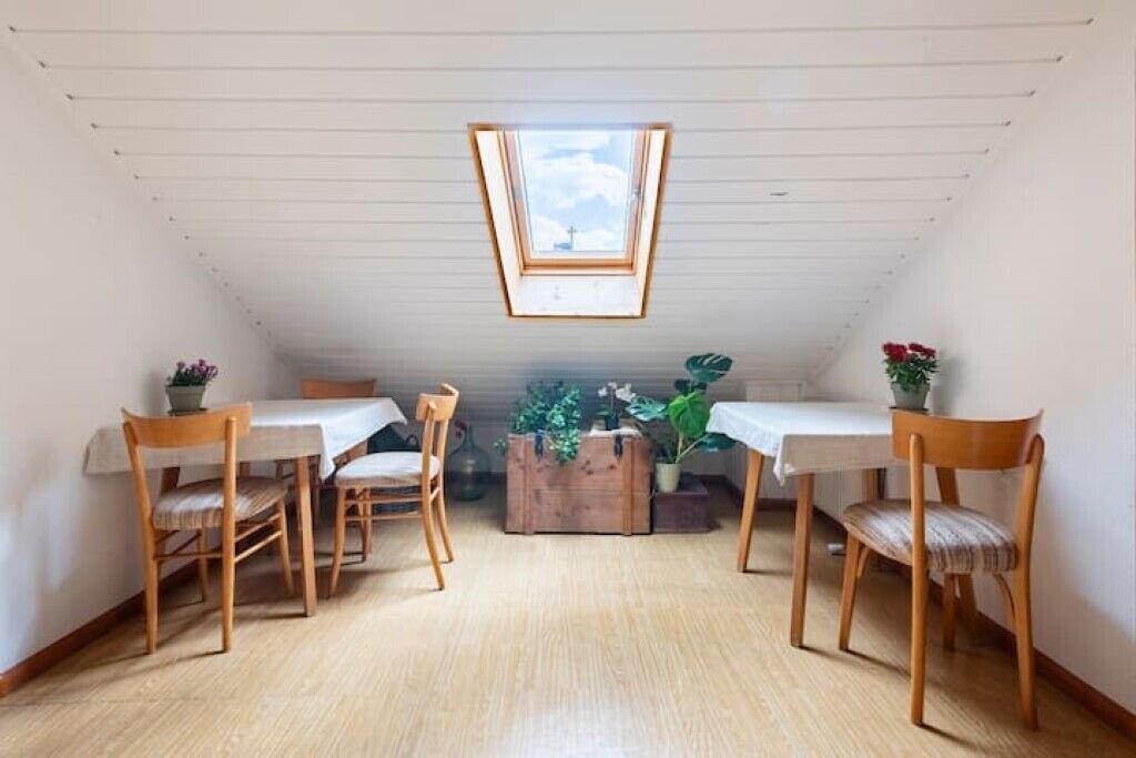 Ein Essbereich mit hoher Decke und Oberlicht, ausgestattet mit Holztischen und -stühlen sowie Blumentöpfen.