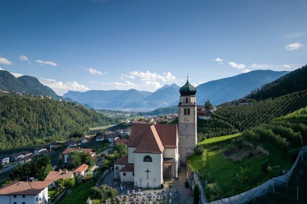 Une église dotée d’un clocher, entourée d’un village et de montagnes.