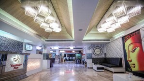 Un vestíbulo de hotel con mostrador de recepción, un reloj y un gran mural de Buda.